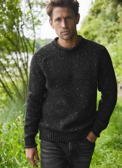 man in grassy pathway wearing black knit sweater with one hand in pocket